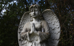 Grey concrete angel statue with praying hands as if in bereavement